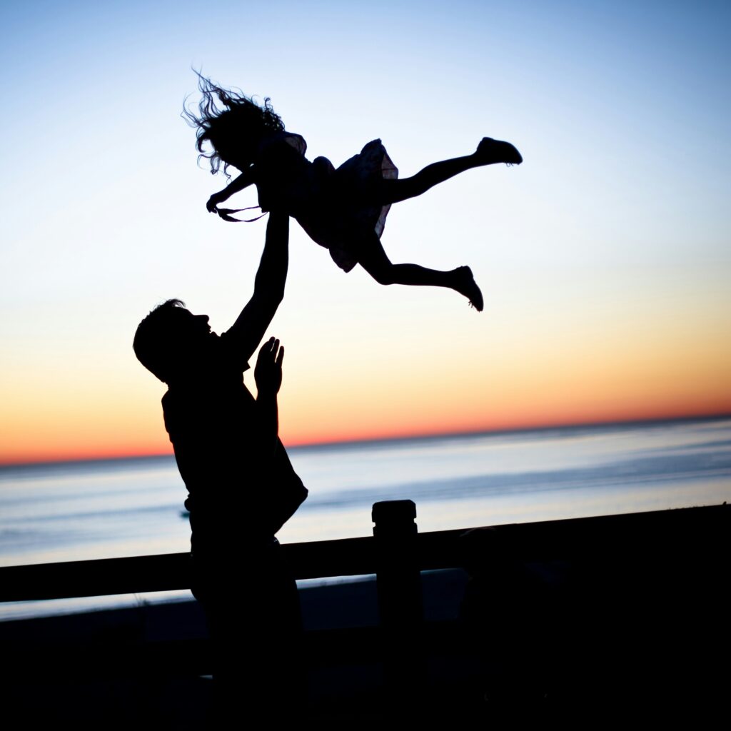 Silhouette of man and child at sunset beach.