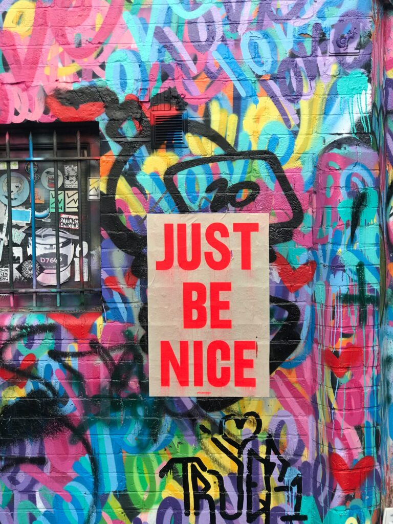 Colorful graffiti wall with 'Just Be Nice' poster.