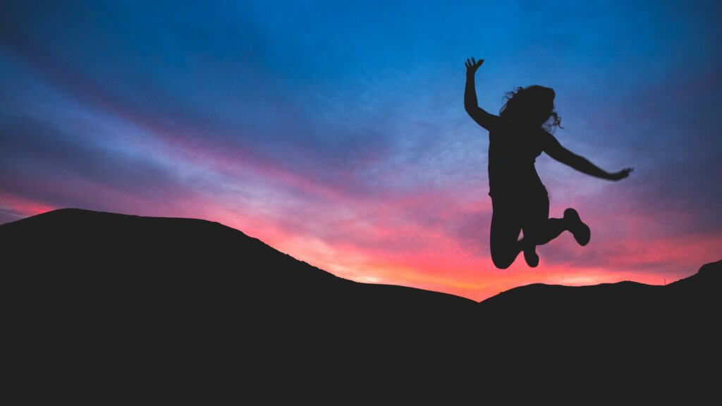 Silhouette jumping against colorful sunset sky.