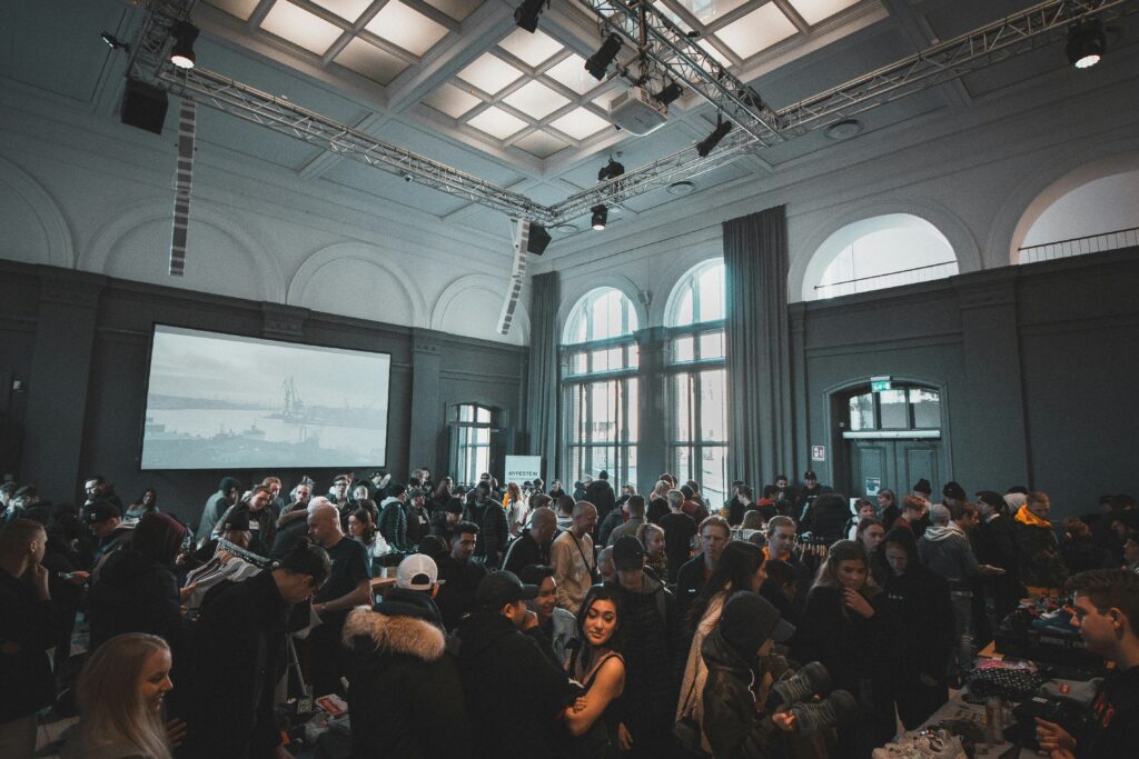 Crowded event in large indoor space with big screen.