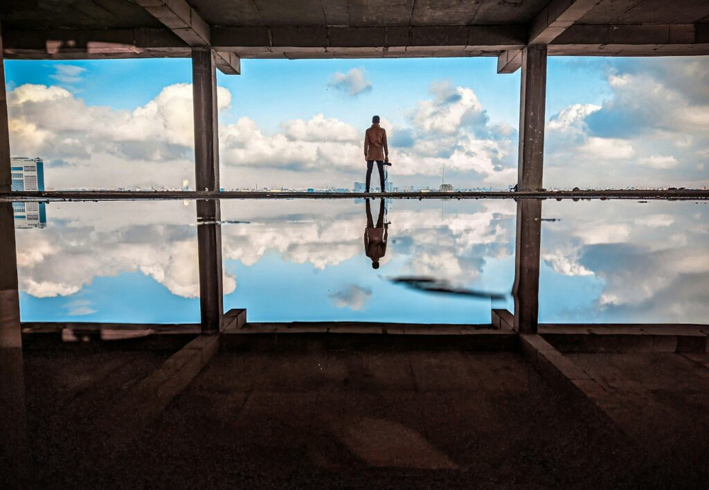 Person standing near water with sky reflection.