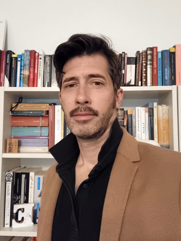 Person in brown blazer in front of bookshelves.